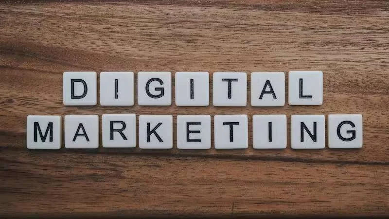 Palavras 'DIGITAL MARKETING' formadas por peças de letras brancas sobre uma superfície de madeira